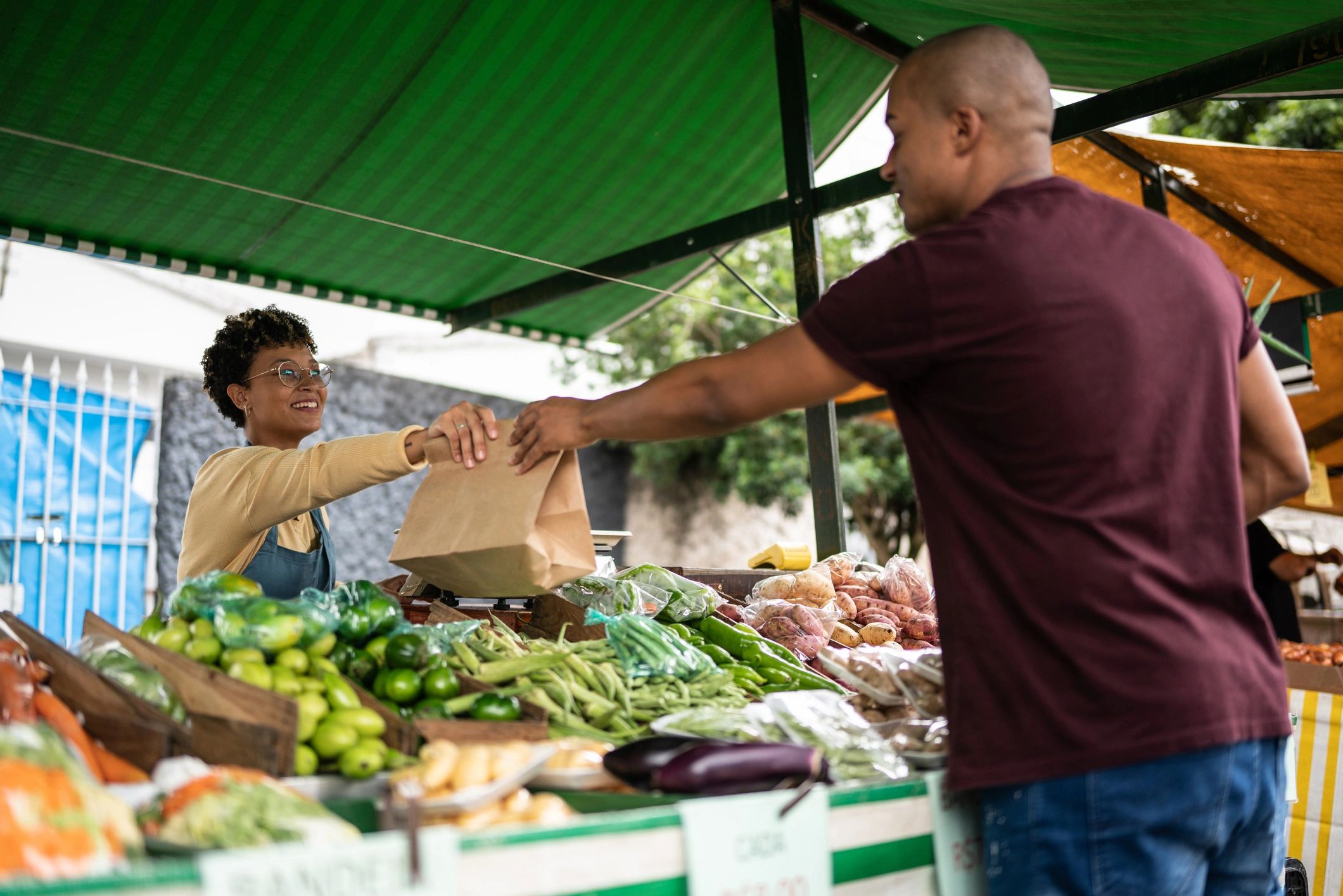 Seller handing a shopping bag to a customer at a street market
