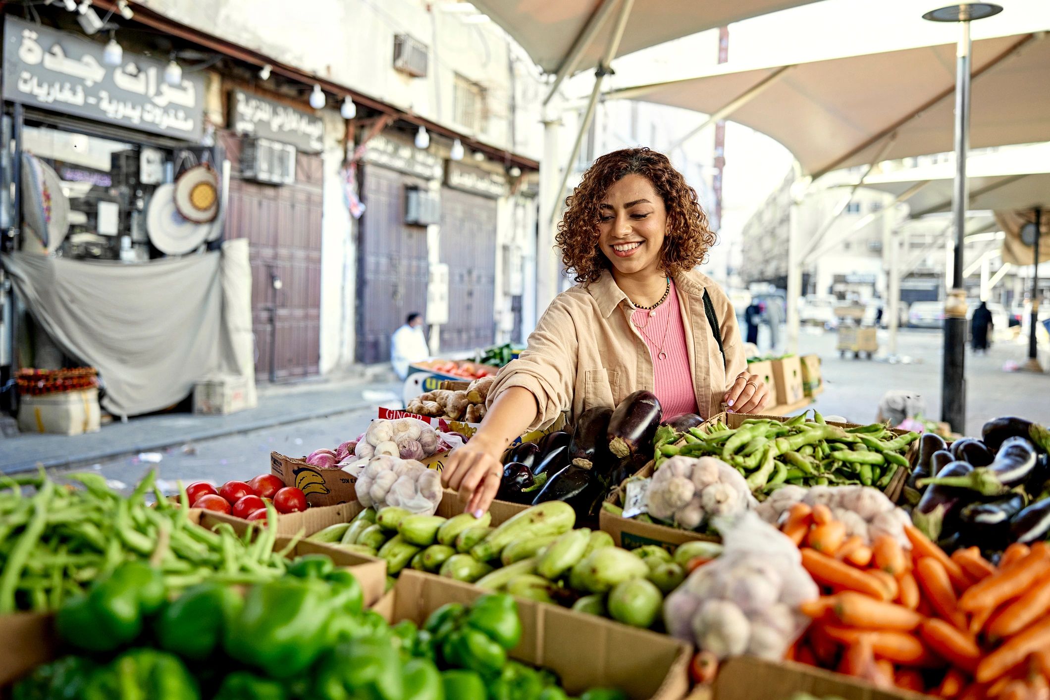Customer selecting zucchini from a vegetable display at an outdoor market
