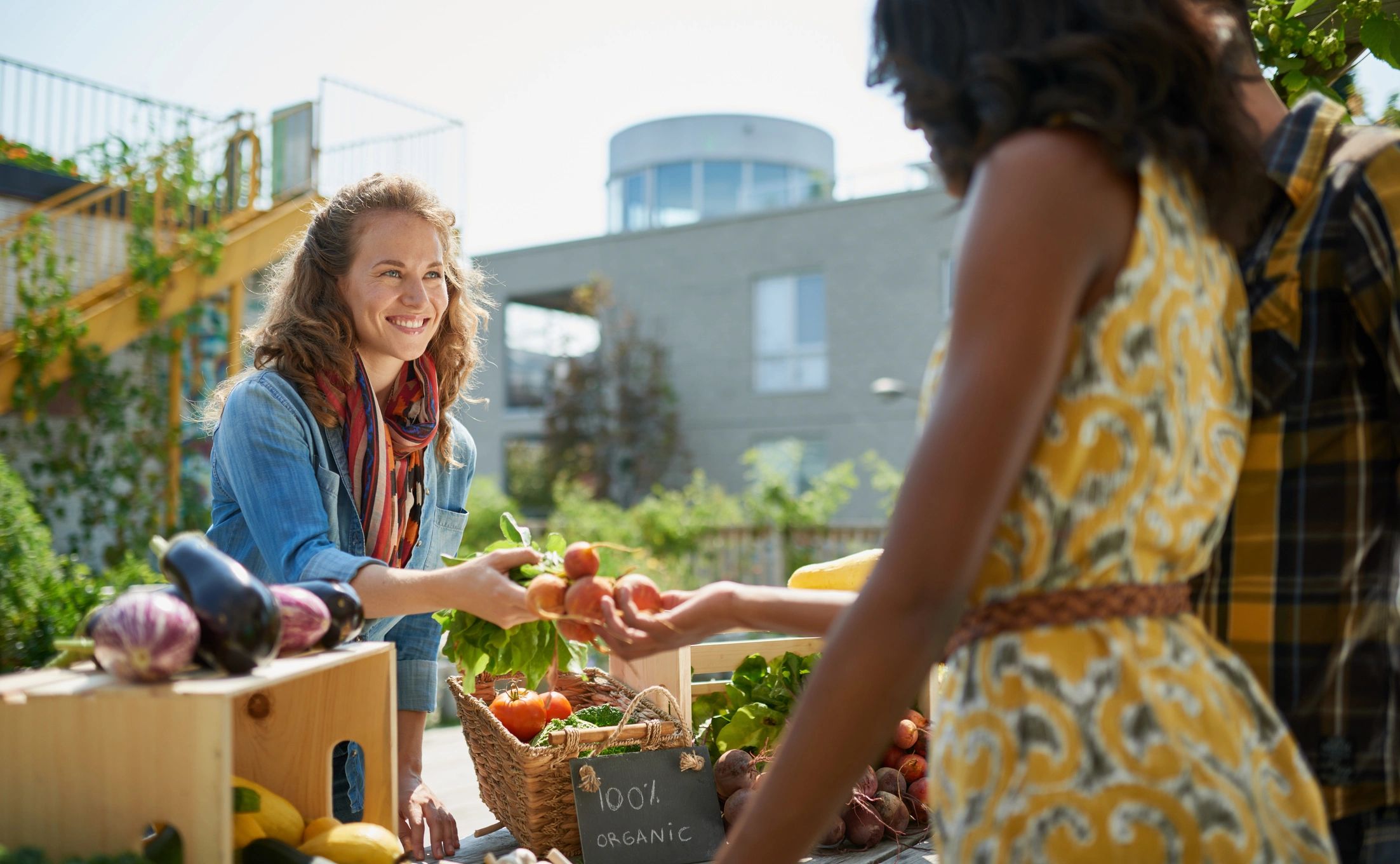 Woman tending an organic vegetable stall with a basket of produce